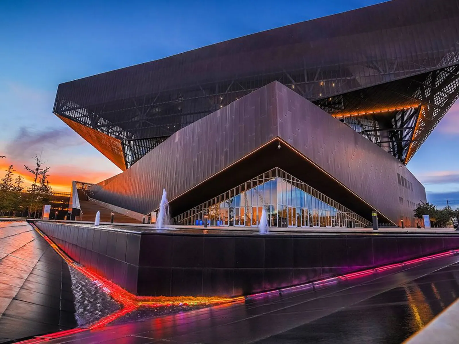 An angular convention venue at dusk with pink light trails